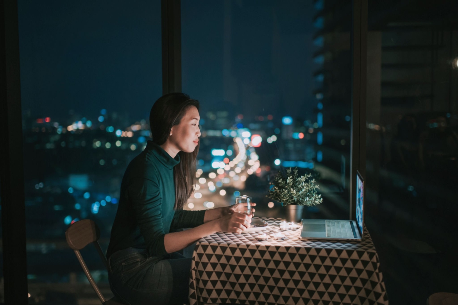 an asian chinese beautiful young lady having dessert in her apartment during magic hour, dusk and talking to her boyfriend thru internet using her laptop